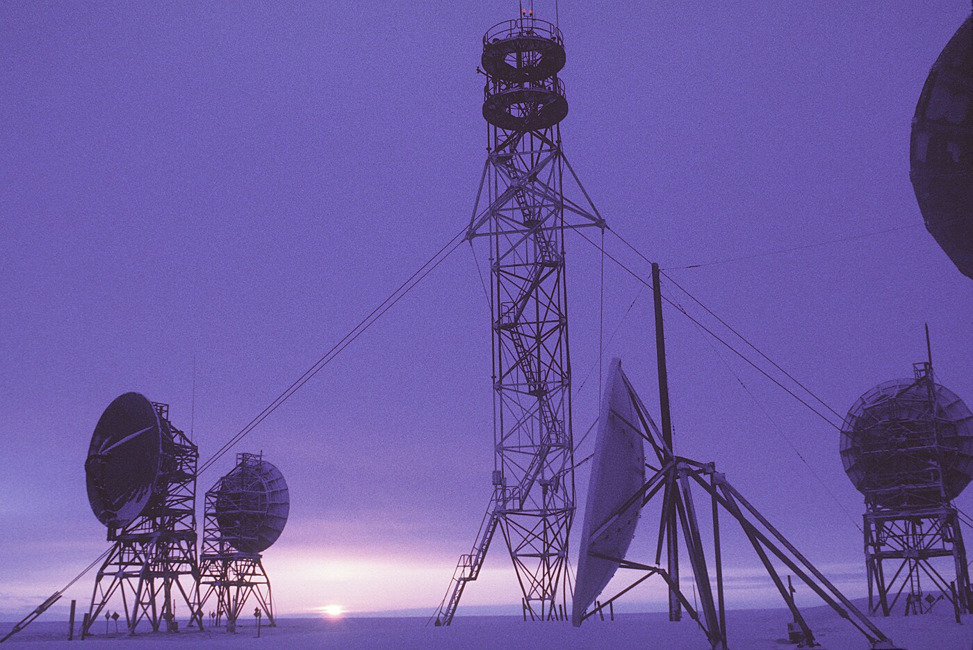 The DEW Line radar station at Barter Island, Alaska at dusk, February 1987 — tropospheric-scatter dish antennas, a lattice communications mast and a radar radome silhouetted against a low Arctic sun.