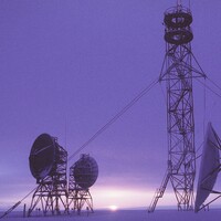 The DEW Line radar station at Barter Island, Alaska at dusk, February 1987 — tropospheric-scatter dish antennas, a lattice communications mast and a radar radome silhouetted against a low Arctic sun.