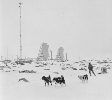 A man and sled dogs, with microwave reflectors in the background